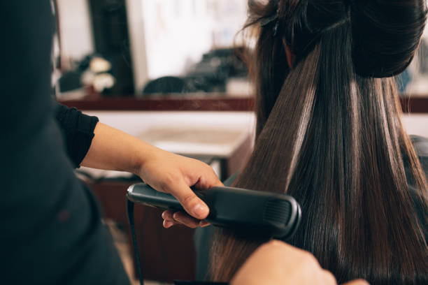 Woman at the hair salon getting her hair styled Hairdresser using a hair straightened to straighten the hair. Hair stylist working on a woman's hair style at salon. adjusting stock pictures, royalty-free photos & images