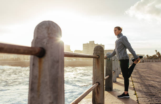 海辺の遊歩道でストレッチをやって女性ランナー - railing beautiful human leg people ストックフォトと画像
