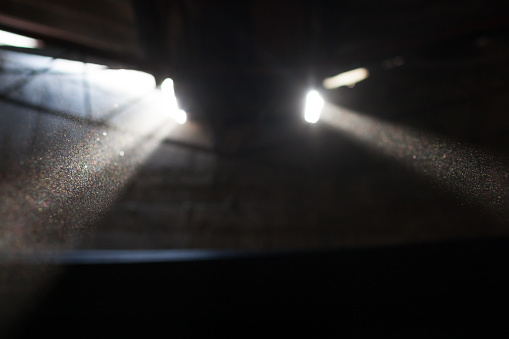light rays protruding from ceiling windows in old dark factory filled with dust particles