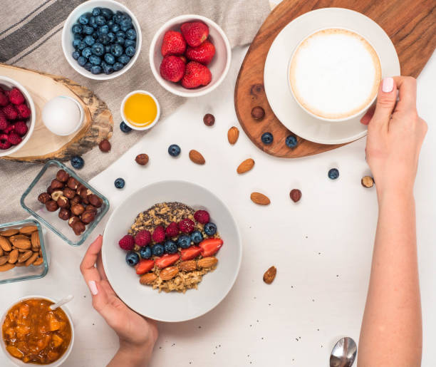 istock Good morning - healthy breakfast background with oatmeal coffee, berries, egg, nuts. Coffee, hands, hold, cup. White wooden food background, top view 851057314