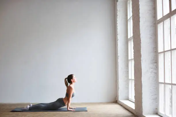Young beautiful woman practicing the cobra pose during yoga class in a gym.