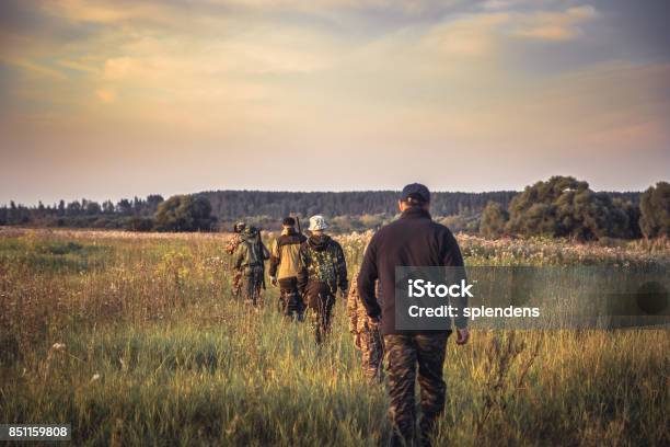 Group Of People In A Row Going Away Through Rural Field At Sunset During Hunting Season In Countryside Stock Photo - Download Image Now