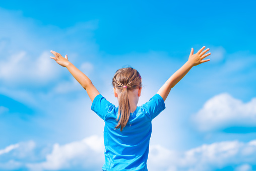 Happy child girl with open arms outdoor under blue sky. Young girl relax outdoors. Freedom concept