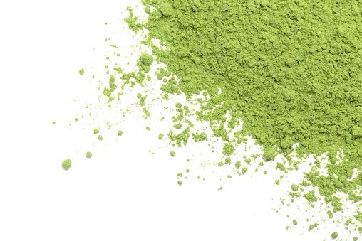 Wheatgrass dried and ground into powder and scattered across a white background.