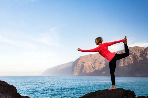 Woman meditating in yoga dancer pose(Natarajasana) over ocean and islands, coastline and rocky mountains. Inspiration and  motivation with healthy lifestyle in beautiful sunset landscape, fitness concept.