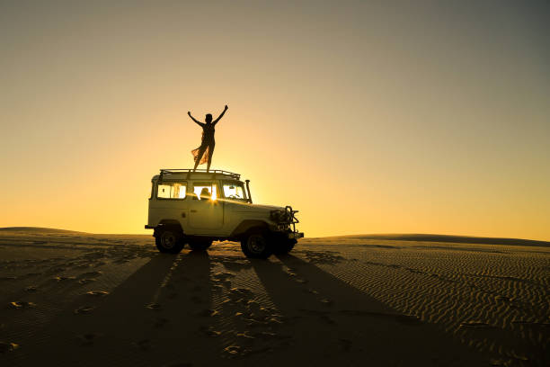 woman celebrating on top of offroad car Woman celebrating the sunset on a top of a offroad car in a desert dirt road sunset stock pictures, royalty-free photos & images