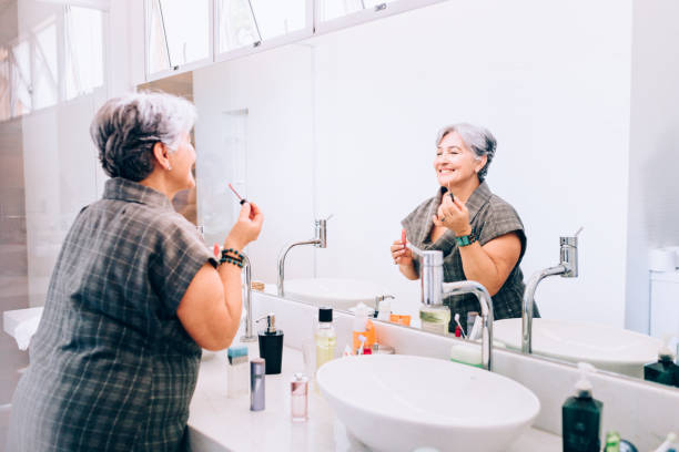 senior woman looking at the mirror using lip brush - mirror vanity women looking imagens e fotografias de stock