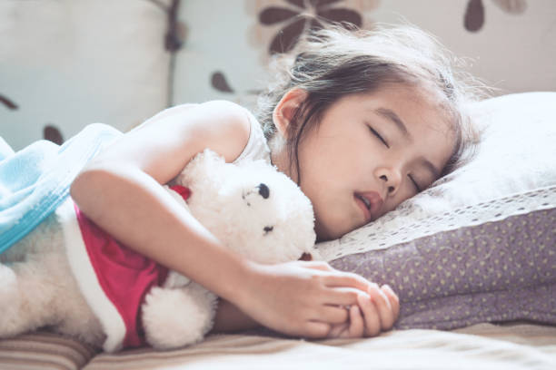 Cute asian child girl sleeping and hugging her teddy bear in the bed stock photo