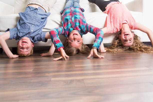 three children, a girl and two boys in white T-shirts and blue jeans, sit hugging each other on the home sofa and smile. the concept of family happiness