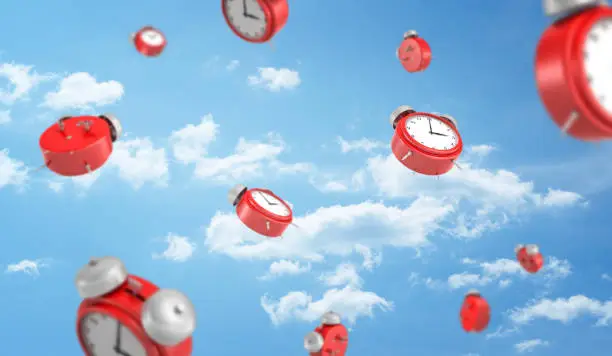 Photo of 3d rendering of a many red retro-looking alarm clocks with metal bells fall down on cloudy sky background