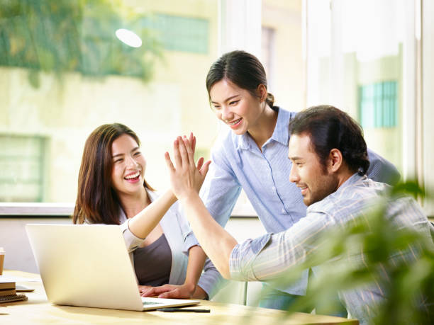 happy asian business team working together in office young asian business person giving coworker high five in office celebrating achievement and success. asian culture stock pictures, royalty-free photos & images