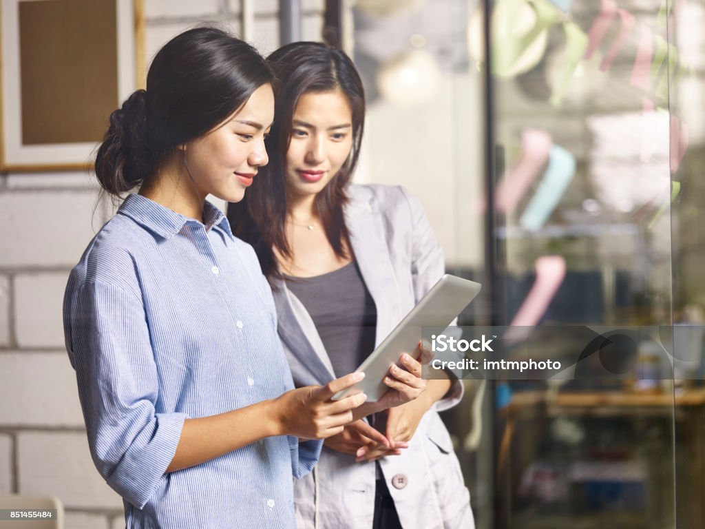 two asian business women working together in office young asian colleagues coworkers working together in company meeting room using digital tablet. Asian and Indian Ethnicities Stock Photo