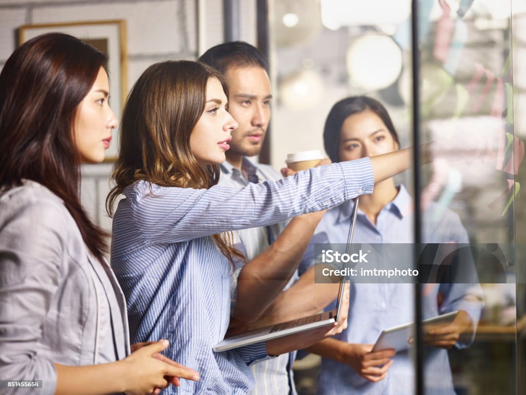 asian and caucasian businesspeople meeting in office a team of asian and caucasian business people working in a brainstorm session using laptop computer, digital tablet and post-it notes. Global Business Stock Photo