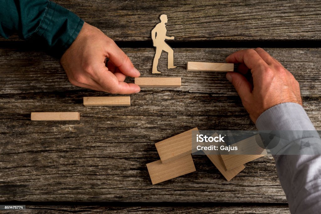 Two people building small toy wood staircase Two unidentifiable adult people building small toy wood staircase as small wooden person walks up the staircase. Ladder of Success Stock Photo