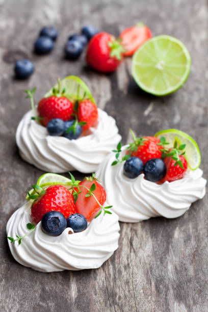 istock Mini  Pavlova meringue cakes with berries and lime on rustic wooden background 851479190