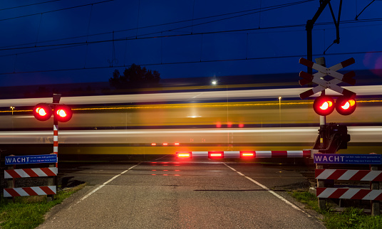 Woudenberg, The Netherlands - August 21, 2017: Yellow and blue NS train with lights passing a railway crossing in the night in the Netherlands.