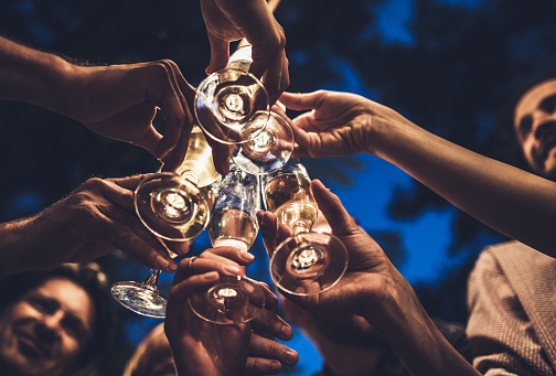 Close up of group of unrecognizable people toasting with champagne on a night party.