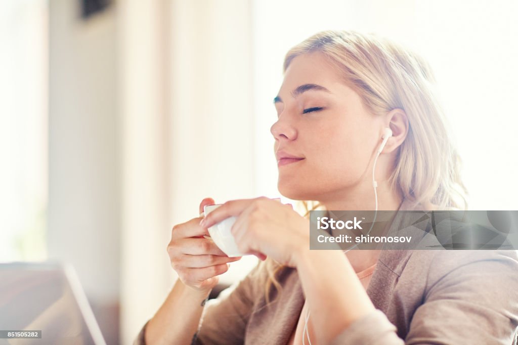 Pleasure at leisure Serene girl with cup of tea listening to her favorite relaxing music at leisure One Woman Only Stock Photo