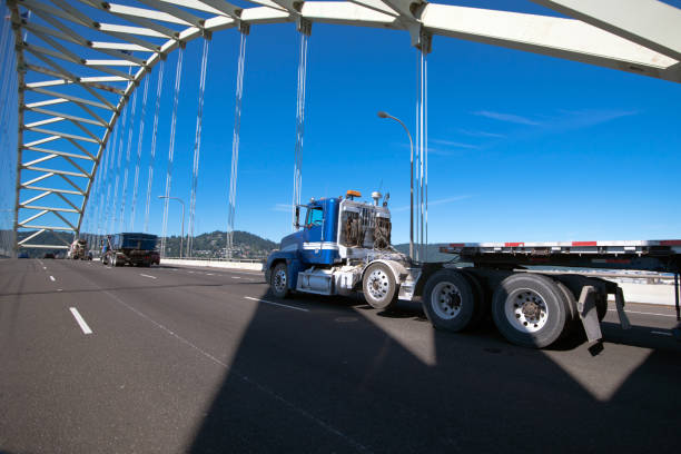 istock Big rig semi truck with long flat bed trailer running on arched truss bridge 851543688