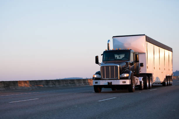 istock Black heavy class big rig semi truck with day cab for local deliveries transport bulk semi trailer with grooved walls on the roadway 851546708