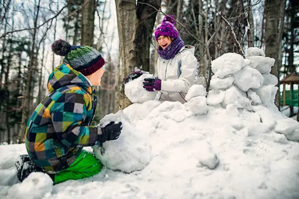 Photo of Brother and sister having fun building a snow fortress in forest