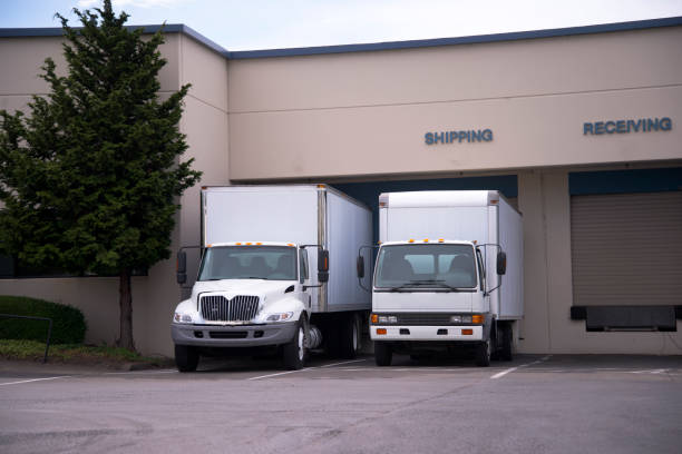 istock Two middle class semi trucks with box trailers stand in dock on shipping receiving departament of warehouse building 851555064