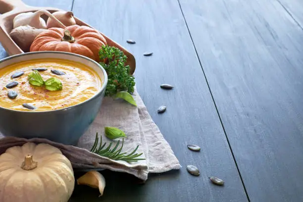 Spicy pumpkin creme soup with ginger, onion and garlic in ceramic bowl on the wooden table. The soup is served with pumpkin seeds and basilicum. Space for your text.