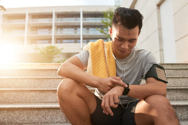Checking fitness tracker Young Vietnamese man checking smartwatch after jogging in the morning fitness tracker photos stock pictures, royalty-free photos & images