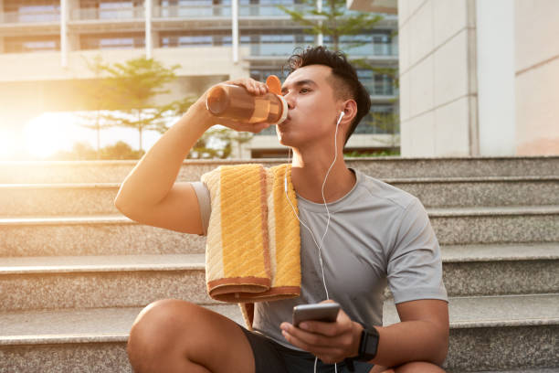Enjoying vitamin drink Handsome Asian man drinking water after outdoor morning jog asian man headphones stock pictures, royalty-free photos & images