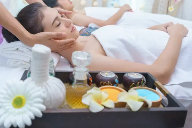 Photo of Beautiful young Asian woman relaxing , lying on massage table and having Thai traditional face massage in spa salon