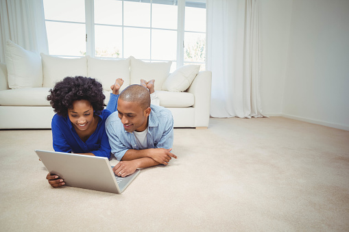 Smiling couple lying on the floor and using laptop
