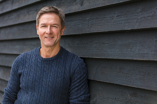 Portrait shot of an attractive, successful and happy smiling middle aged man male outside wearing a blue sweater