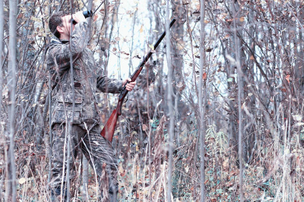 A man in camouflage and with a hunting rifle in a forest on a sp