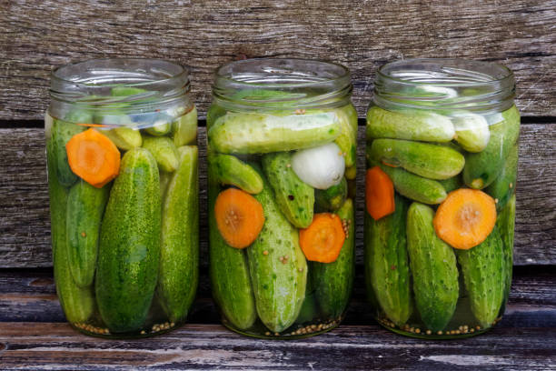 istock Three open glass jars of pickled cucumbers  on rustic wooden board. 851767668