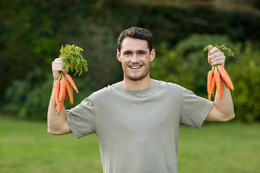 Portrait of young man holding bunch of freshly plucked carrots in both the hands