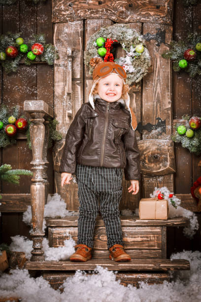 istock Little two year old boy dressed in braun leather jacket, pants and boots with pilot hat on posing in christmas decorations 851779060