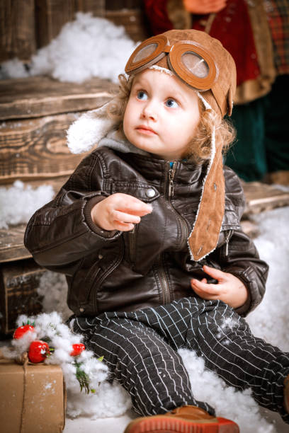 istock Little two year old boy dressed in braun leather jacket, pants and boots with pilot hat on posing plays with snow in christmas wooden decorations 851780216