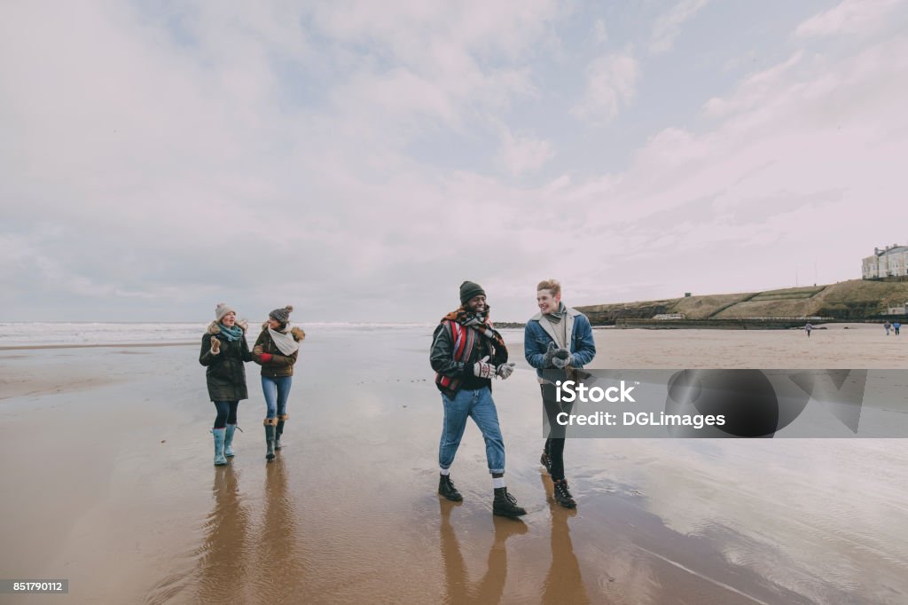 A Group Of Friends Walk Along A Winter Beach A group of teenagers talk and laugh together whilst walking along a winter beach. UK Stock Photo