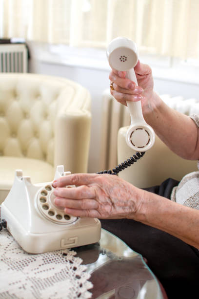 レトロなケーブル電話の電話番号をダイヤルしわの年配の女性の手のクローズ アップ。 - landline phone women close up old fashioned ストックフォトと画像