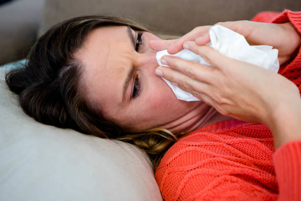 istock sick woman blowing her nose into a tissue 851830444