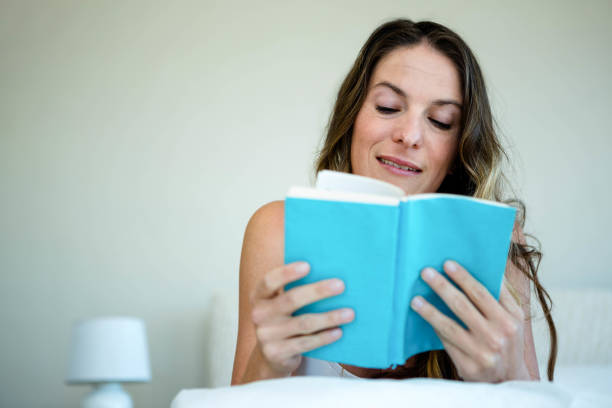 istock smiling woman reading a book in bed 851843834