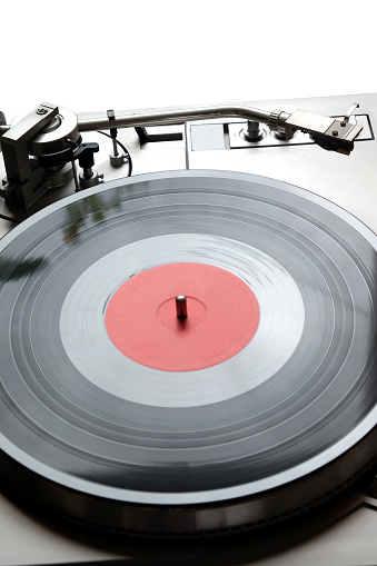 Vintage turntable in silver case with buttons and knobs on control panel with vinyl record with red label isolated on white background. top view closeup
