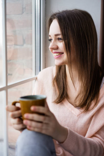 istock Young woman sitting at window drinking coffee 851862838