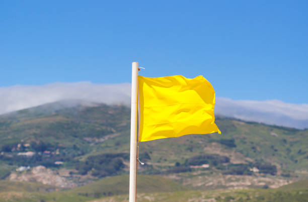 gelbe fähnchen in der brise vor einem unscharfen blauen himmel am strand. - traditional sport sports flag golf flag golf stock-fotos und bilder