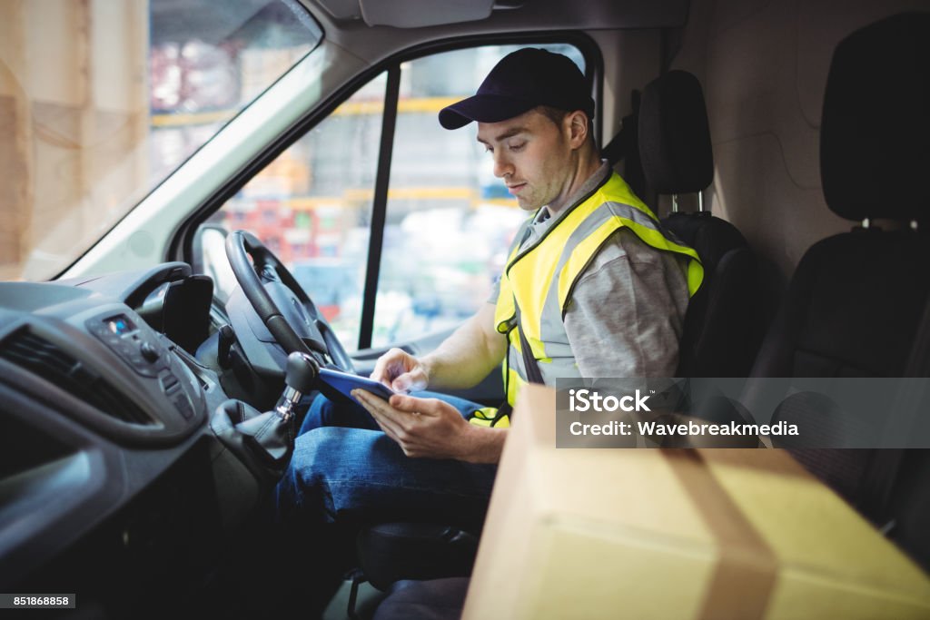 Delivery driver using tablet in van with parcels on seat Delivery driver using tablet in van with parcels on seat outside warehouse Delivery Person Stock Photo