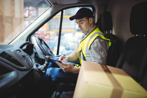 Delivery driver using tablet in van with parcels on seat Delivery driver using tablet in van with parcels on seat outside warehouse delivery person stock pictures, royalty-free photos & images