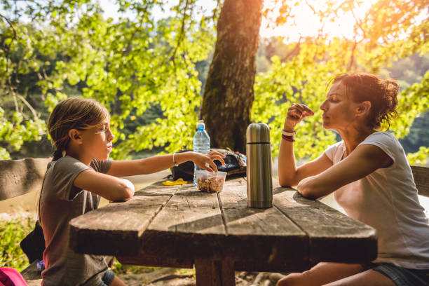 Mother and daughter eating at a picnic table Mother and daughter eating healthy snack at a picnic table in the forest bottled water on table stock pictures, royalty-free photos & images