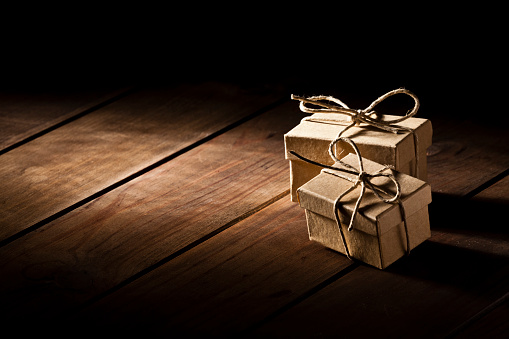 Horizontal view of two brown gift boxes shot on rustic wood table. The boxes are tied up with a rope ribbon. The two boxes are grouped at the right side of the frame leaving a useful copy space ready for text and/or logo at the left. Predominant color is brown. DSRL studio photo taken with Canon EOS 5D Mk II and Canon EF 70-200mm f/2.8L IS II USM Telephoto Zoom Lens