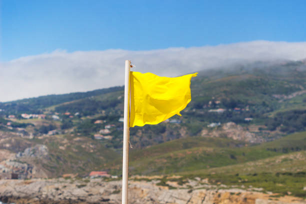 gelbe fähnchen in der brise vor einem unscharfen blauen himmel am strand. - traditional sport sports flag golf flag golf stock-fotos und bilder