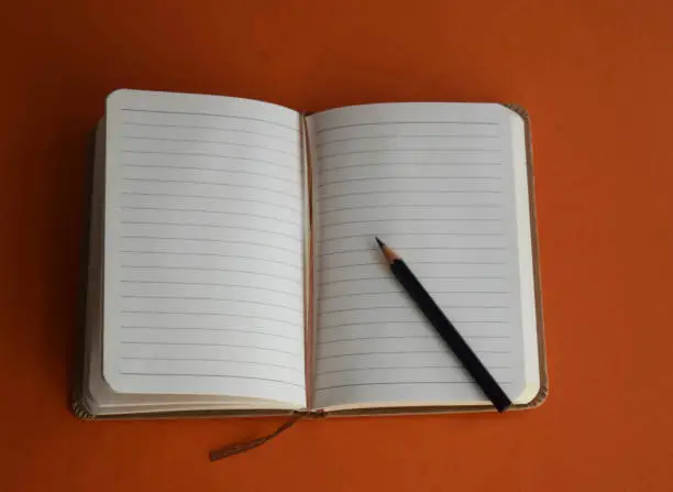Pencil and notebook-paper on the orange background